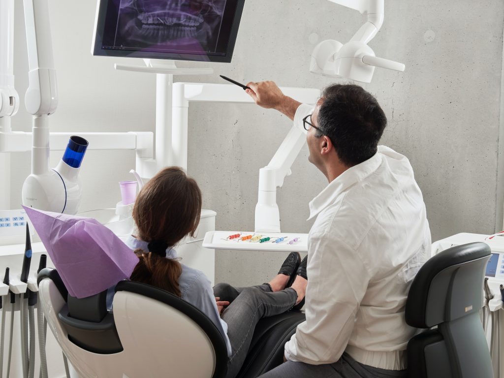 A dentist points to an x-ray while discussing with a patient